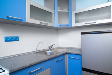 Interior of kitchen is blue. Metal sink with faucet.