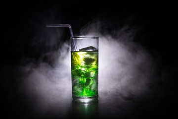 Cocktail glass splashing on dark toned smoky background or colorful cocktail in glass. Party club entertainment. Mixed light.