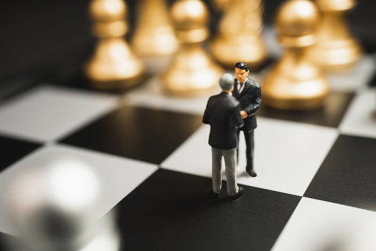 Miniature business partnership handshake concept. Successful businessmen handshaking after good deal on gold and silver chess background.