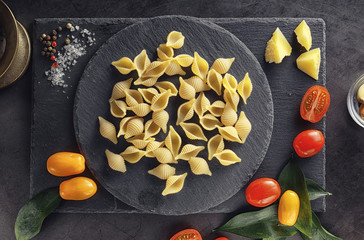 Pasta shells on black stone. Tomatoes and bay leaves with allspice and sea salt.