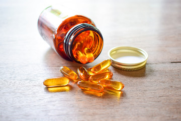 Omega 3 fish oil pills spread out from brown bottle over the wooden table