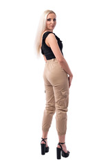 Fototapeta premium Back view of serious confident blonde woman with attitude in stylish clothes turning and looking at camera. Full body isolated on white background. 