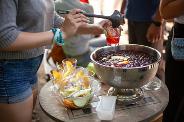 The girl pours a punch into a glass. Party in the open air. Light alcoholic drinks for friends. Rest in the city with drinks.
