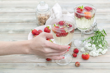 Champagne and strawberries. Female hand holds a glass with champagne and strawberries. Summer food composition on a wooden table.