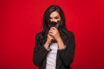 Girl holding makeup brushes on red background