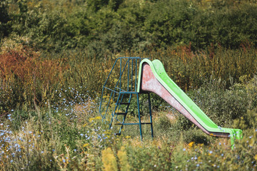 Old abandoned children plastic slide among heavy vegetation