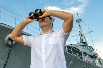 Navy officer standing beside warship and looking around with binocular.
