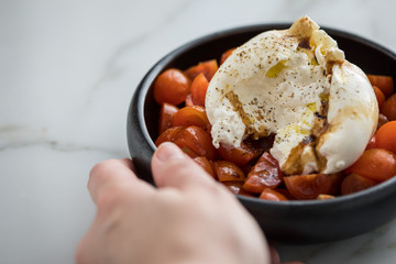 Frau isst Burrata Büffelmozzarella Kugel mit Tomaten, Olivenöl und Balsamico auf schwarzen Teller
