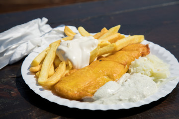 Seelachs Backfisch im Bierteig mit Remoulade, Pommes, Mayonnaise und Krautsalat draußen auf Pappteller und Holztisch 