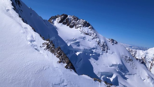Aerial shot passing low over the Dufourspitze summit revealing Margherita mountain hut and Italy in the clouds in background. Highest peak in Switzerland, Monte Rosa area, Zermatt.