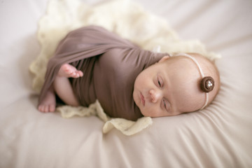 Obraz na płótnie Canvas sleeping newborn baby in a wrap brown blanket on the bed