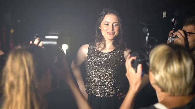 Famous woman in shiny dress posing in front of paparazzi cameras, evening party