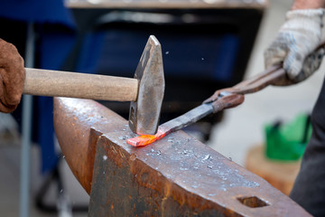 Unrecognizable blacksmith forging red-hot metal with hammer. Blacksmithing concept.