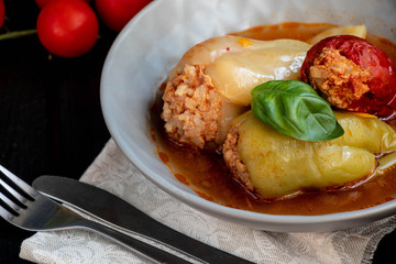 Dietary pepper stuffed with chicken breast and rice with vegetables. In tomato sauce. Near raw peppers and cherry tomatoes. On a dark background. 