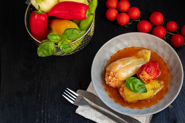 Dietary pepper stuffed with chicken breast and rice with vegetables. In tomato sauce. Near raw peppers and cherry tomatoes. On a dark background. 