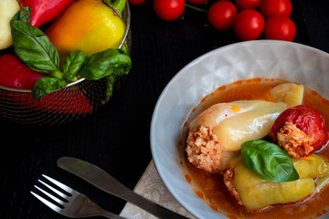 Dietary pepper stuffed with chicken breast and rice with vegetables. In tomato sauce. Near raw peppers and cherry tomatoes. On a dark background. 