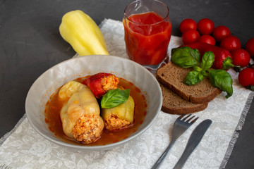 Dietary pepper stuffed with chicken breast and rice with vegetables. In tomato sauce. Near raw peppers and cherry tomatoes. On a dark background. 