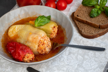Dietary pepper stuffed with chicken breast and rice with vegetables. In tomato sauce. Near raw peppers and cherry tomatoes. On a dark background. 