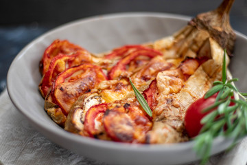 Dietary fan of eggplant white filled with tomatoes and cheese. Nearby are cherry tomatoes, rosemary branches. It is worth soy sauce and metal appliances. On a dark background.