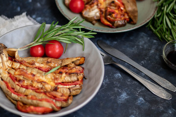 Dietary fan of eggplant white filled with tomatoes and cheese. Nearby are cherry tomatoes, rosemary branches. It is worth soy sauce and metal appliances. On a dark background.