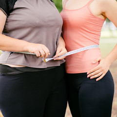 Overweight and fit women standing together wrapped with measure tape. Dieting, group weight loss and health care concept