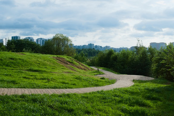 Beautiful landscape with green grass and modern buildings. The path is hidden behind the hill.