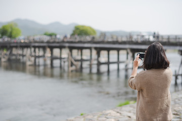 Young Asian woman short hair tourist is taking a picture by camera at Togetsu-kyo Bridge in Arashiyama district, Kyoto, Japan. Travel in Japan concept.