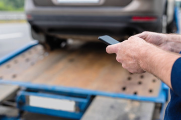 Man with mobile phone.Tow truck with worker towing a broken down car on the highway. Selective focus. Concept