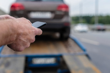 Naklejka premium Man with mobile phone.Tow truck with worker towing a broken down car on the highway. Selective focus. Concept
