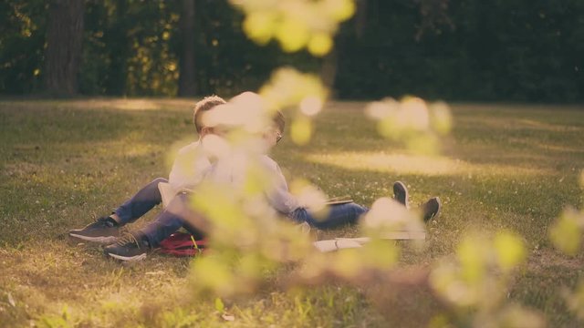 cute happy diligent kids in shirts prepare for school test with books sitting on lush grass in green school garden