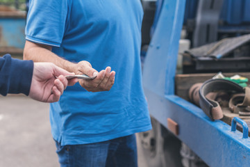 Man pays paper money for tow truck to worker towing a broken down car. Selective focus. Concept
