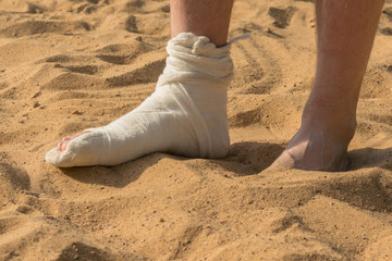 Human legs in the sands of the desert. One leg is plastered. The second leg is barefoot, immersed...