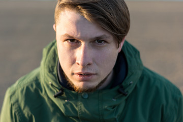 Dramatic portrait of a young man on the street. Green windbreaker. Fashionable long haircut. Confident, deep, thoughtful look.