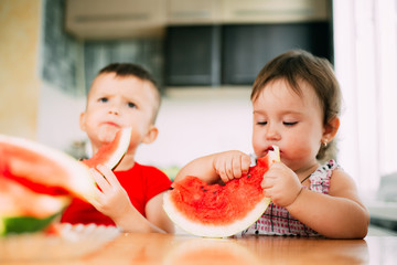 Children, brother and sister, boy and girl in the kitchen eating watermelon, a lot of fun