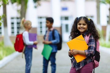 Back to school. Close up Three Friends With Backpacks huging and laughing in front of school. Mixed Racial Group of School Kids having fun in the schoolyard.