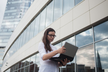 Fototapeta premium Career growth and ambitions, concept. Young businesswoman with a laptopon the background of the business center.
