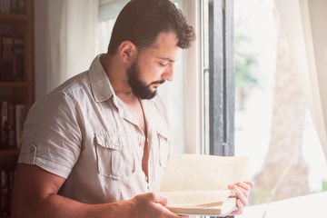 bearded man reading book near to window