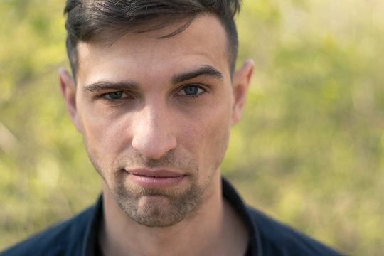 dramatic portrait of a young, brutal-looking man. Close-up. Fashionable hairstyle and manly bristles. Wearing a black leather jacket. The face expresses the emotion of "mock, malevolent smile."