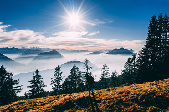 aerial view of guy looking at mountain scenery in the swiss alps during late autumn, colored pinetrees and blue Lake Lucerne covered in fog seen from rigi switzerland