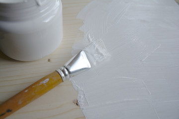 Plastic can with white acrylic primer and a bristle brush on a wooden panel. Preparing the surface...