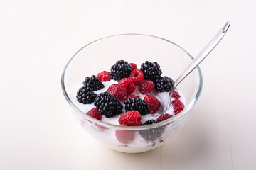 Ice cream with raspberry, blackberry berries with spoon in glass bowl on white background