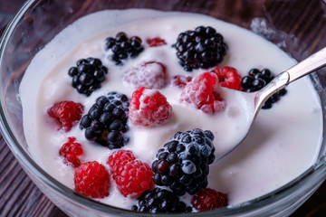Ice cream with raspberry, blackberry berries with spoon in glass bowl on dark wooden background