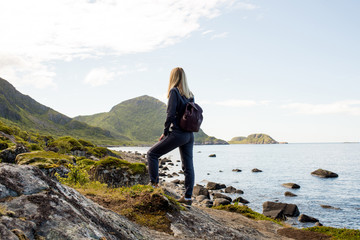 Obraz premium Woman goes on tourist hiking trail along ocean and mountains in Norway. Active recreation, healthy lifestyle. Enjoys scenic view. Beautiful nature. Travel, adventure. Sense of freedom. Explore North