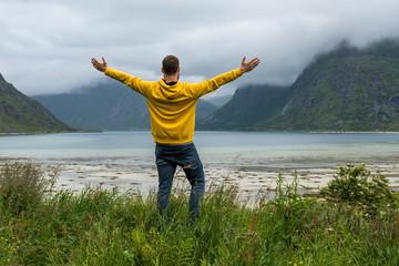 Men in yellow hoodie outdoor enjoys the scenic view of the fjord. Stunning beauty nature. Harmony, relax lifestyle. Travel, adventure. Sense of freedom. Explore North Norway. Summer in Scandinavia