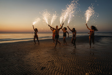 Group of friends having fun running on the beach with sparklers