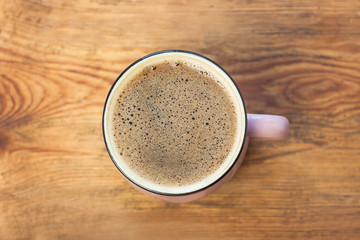 A cup of coffee on wooden background. Beautiful foam, pink ceramic mug, stylish toning, copy space.