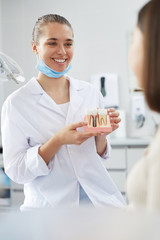 Portrait of smiling female dentist holding tooth model while consulting patient in clinic, copy space