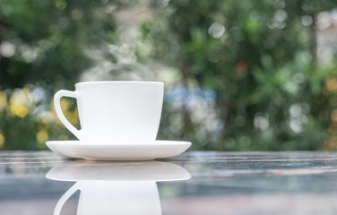 A cup of hot coffee in white cup with steaming at garden in coffee shop