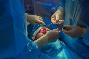 Surgeon and his assistant performing cosmetic surgery on nose in hospital operating room. Nose reshaping, augmentation. Rhinoplasty.