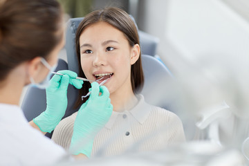 High angle portrait of smiling Asian girl sitting in dental chair during check up, copy space